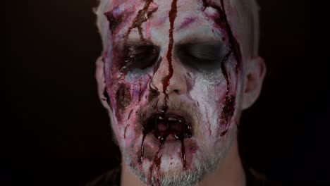 Close-up-of-sinister-man-with-horrible-scary-Halloween-zombie-make-up-blood-flows-and-drips-on-face