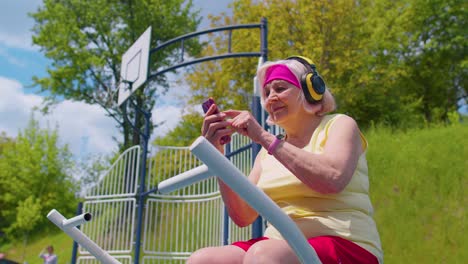 Senior-woman-after-sport-training-listening-music-on-playground,-celebrate-win-doing-winner-gesture