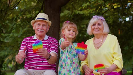 Senior-grandmother-grandfather-with-granddaughter-holding-anti-stress-pop-it-toy-games-in-park