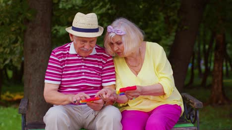 Stylish-senior-grandmother-grandfather-playing-squeezing-anti-stress-toy-simple-dimple-game-in-park