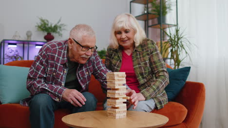 Älterer-Alter-Großeltern-Mann-Frau,-Der-In-Blöcken-Spielt,-Holzturm-Baut-Brettspiel-Auf-Dem-Tisch-Zu-Hause