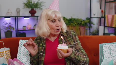 Happy-senior-elderly-grandmother-woman-celebrating-birthday-party,-makes-wish-blowing-burning-candle