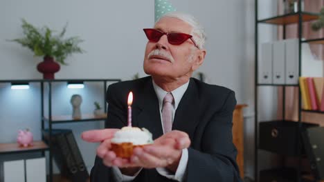 Un-Hombre-De-Negocios-Senior-Celebrando-Un-Cumpleaños-Solitario-En-El-Cargo,-Soplando-Una-Vela-En-Un-Pastel-Pequeño-Pidiendo-Un-Deseo