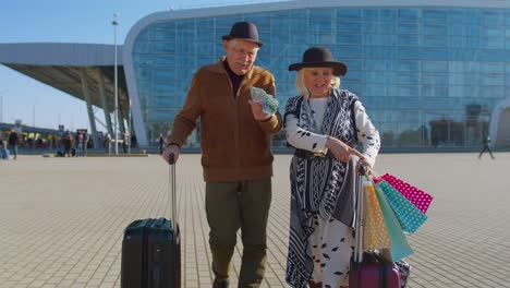 Senior-rich-pensioner-tourists-walking-with-shopping-bags-from-vacation-holding-dollar-money-cash