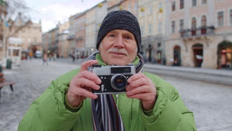 Senior-man-taking-pictures-with-photo-camera,-using-retro-device-outdoors-in-winter-city-center
