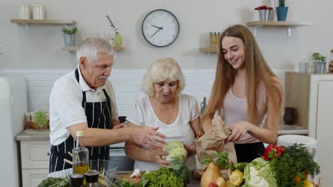 Elderly-couple-in-kitchen-receiving-vegetables-from-grandchild.-Raw-food-healthy-eating-diet
