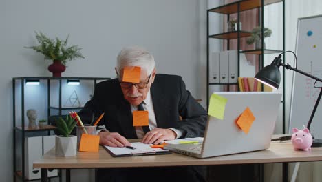 Tired-exhausted-senior-business-man-office-manager-with-laptop-sticky-notes-sticks-with-many-tasks