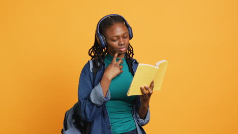 Young-girl-wearing-headphones-reading-interesting-book,-studio-background