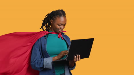 Young-girl-wearing-superhero-for-Halloween-working-on-laptop,-studio-background