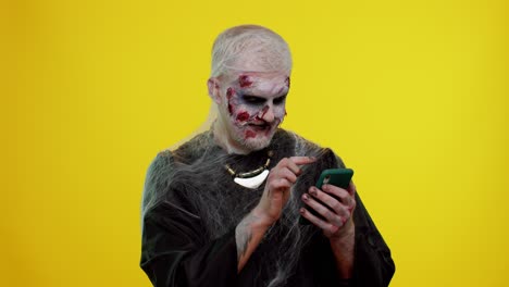 Frightening-man-Halloween-zombie-using-mobile-phone-typing-new-post-on-web,-browsing,-addiction