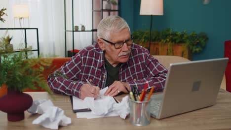 Grandfather-working-on-laptop-man-writing-on-paper-sheet,-getting-angry,-crumpling-it,-throwing-away