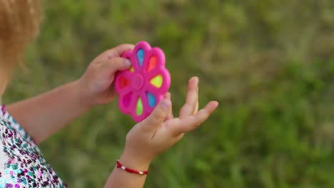 Close-up-of-girl-playing-spinning-with-pop-it-sensory-anti-stress-toy-in-park,-stress-anxiety-relief