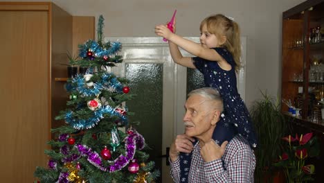 Children-girl-and-elderly-grandpa-decorating-artificial-Christmas-pine-tree-at-old-fashion-room-home