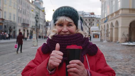 Senior-woman-grandmother-tourist-smiling,-showing-thumb-up-in-winter-city-center-of-Lviv,-Ukraine