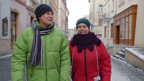 Senior-elderly-couple-tourists-man-woman-walking-along-street-in-winter-city,-enjoying-time-together