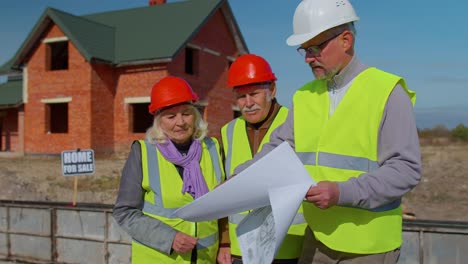 Real-estate-agent-selling-new-house-to-senior-grandmother-grandfather,-showing-building-blueprints