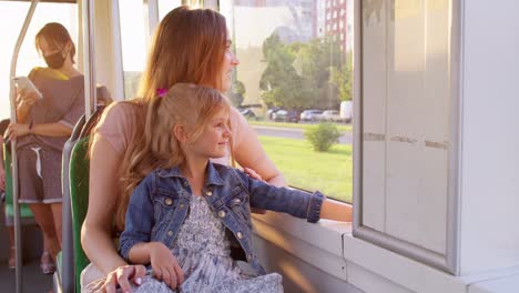 Familie-Fährt-Mit-öffentlichen-Verkehrsmitteln,-Frau-Und-Kleines-Mädchen-Sitzen-Zusammen-Und-Schauen-Aus-Dem-Straßenbahnfenster