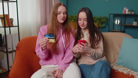 Cheerful-girls-friends-using-credit-bank-card-and-smartphone-while-transferring-money,-purchases