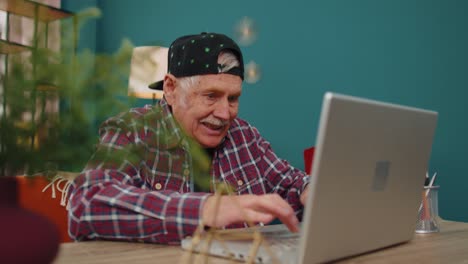 Grandfather-man-playing-computer-video-games-on-laptop-computer,-wins,-celebrate,-smiles-happily