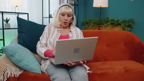 Senior-woman-freelance-wear-headphone-make-video-call-talking,-teaching-at-laptop-at-home-office