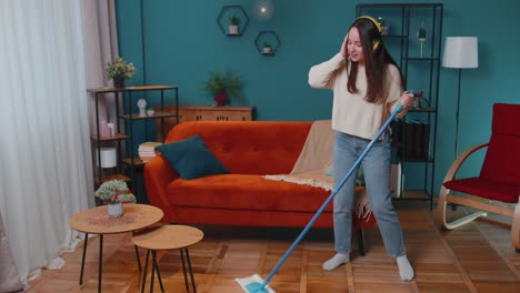 Housekeeper-young-woman-is-mopping-floor-in-apartment-living-room-dancing-listening-to-music-at-home