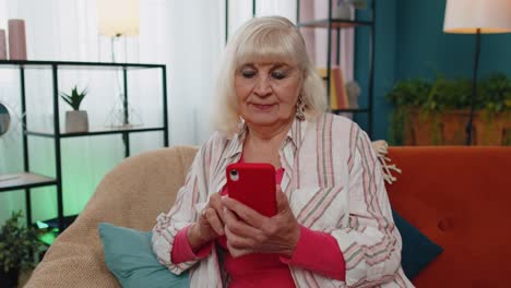 Senior-old-grandparent-works-on-mobile-phone,-sends-messages,-makes-online-purchases-at-home-sofa