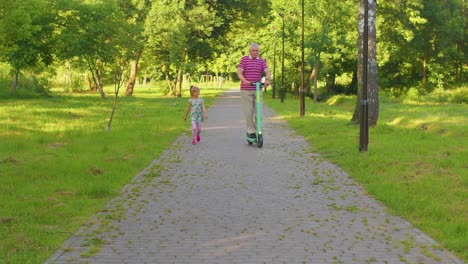 Senior-man-grandfather-tourist-riding-electric-scooter-with-granddaughter-child-girl-in-summer-park
