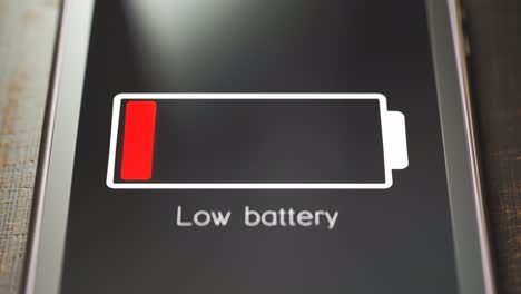 Smartphone-screen-showing-notification-about-low-battery-status.-A-warning-message-with-flashing-battery-symbol-about-low-battery-power-or-exhaustion.-Close-up-of-generic-smartphone-on-wooden-desk.