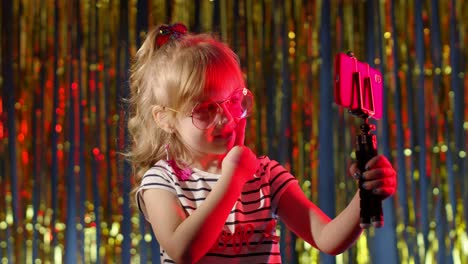 Child-kid-blogger-smiling,-recording-video-blog-vlog-on-smartphone-in-night-club-with-red-neon-light