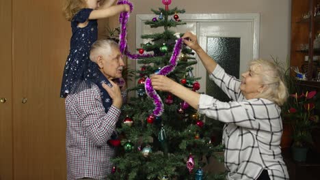 Kinder,-Mädchen-Mit-älteren-Großeltern,-Die-Zu-Hause-Einen-Künstlichen-Weihnachtsbaum-Schmücken