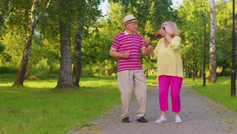 Senior-stylish-couple-grandmother-grandfather-dancing,-listening-music-on-musical-speakers-in-park