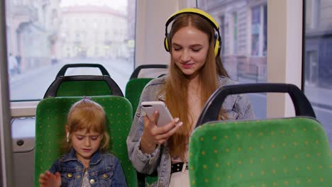 Child-girl-with-mother-using-smartphone-with-headphones,-earphones-listening-music,-funny-dancing