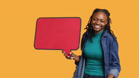Smiling-woman-holding-red-speech-bubble-sign,-studio-background