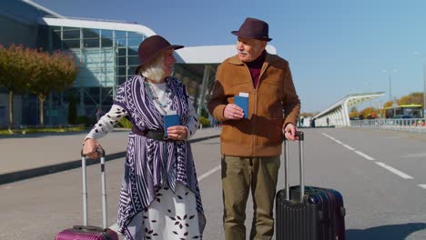 Senior-pensioner-tourists-grandmother-grandfather-stay-from-airport-hall-with-luggage-on-wheels