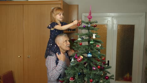 Kleines-Mädchen-Mit-Großen-Großeltern,-Die-Einen-Künstlichen-Weihnachtsbaum-Im-Altmodischen-Zuhause-Schmücken