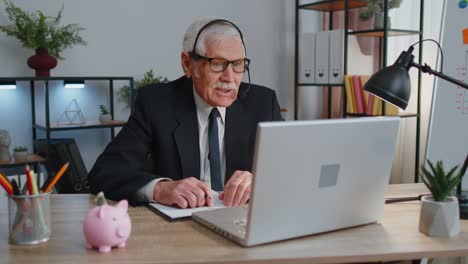 Senior-businessman-in-headphones-making-conference-video-call-on-laptop,-call-center-agent,-operator