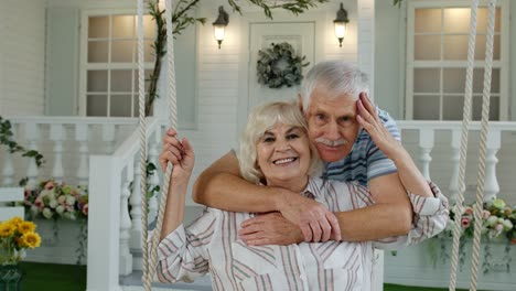 Senior-couple-together-in-front-yard-at-home.-Man-swinging-and-hugging-woman.-Happy-mature-family
