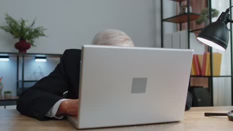 Senior-mature-older-business-man-hiding-behind-laptop-computer,-making-funny-face,-fooling-around