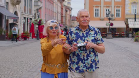 Elderly-stylish-tourists-man-and-woman-taking-photos-with-old-film-camera,-walking-along-city-street