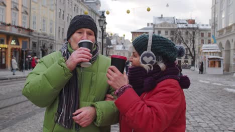 Senior-old-couple-tourists-grandmother-grandfather-traveling,-drinking-hot-drink-tea-in-city-center