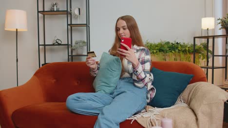 Woman-sitting-at-home-using-credit-bank-card-and-smartphone-while-transferring-money-online-shopping