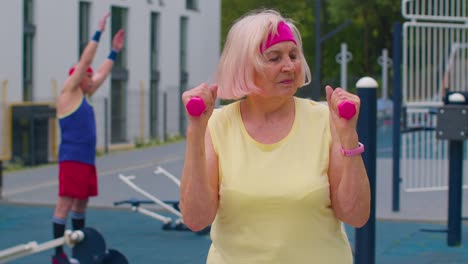 Senior-mature-woman-grandmother-doing-training-weightlifting-exercising-with-dumbbells-on-playground