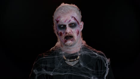 Sinister-man-with-horrible-scary-Halloween-dead-zombie-makeup-in-costume-looking-ominous-at-camera