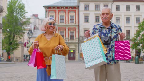 Senior-couple-grandmother-grandfather-tourists-with-bags-after-shopping-in-mall-during-Black-Friday