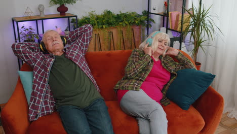Glückliche-ältere-Familie-Großeltern-Mann-Frau-In-Kopfhörern-Musik-Hören-Entspannt-Auf-Der-Couch-Zu-Hause