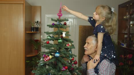 Little-child-girl-and-senior-grandfather-decorating-artificial-Christmas-tree-at-home,-slow-motion