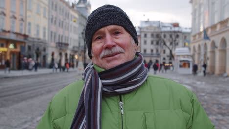 Portrait-of-old-senior-man-tourist-smiling,-looking-at-camera-in-winter-city-center-of-Lviv,-Ukraine