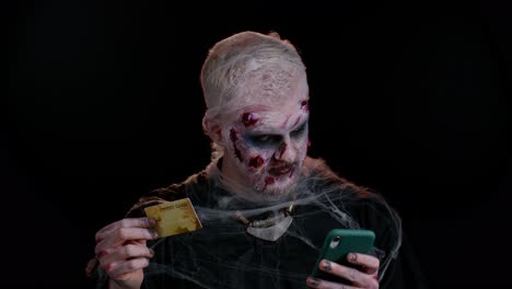 Unheimlicher-Mann-Halloween-Zombie-Mit-Kreditkarte-Und-Smartphone-Beim-Online-Einkauf