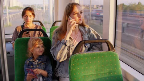 Parent-mother-talking-on-mobile-phone,-ignoring-little-child-daughter-while-sitting-in-public-tram