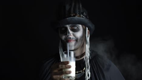 Scary-guy-in-carnival-costume-of-Halloween-skeleton-looking-at-camera,-drinks-milk-from-a-glass